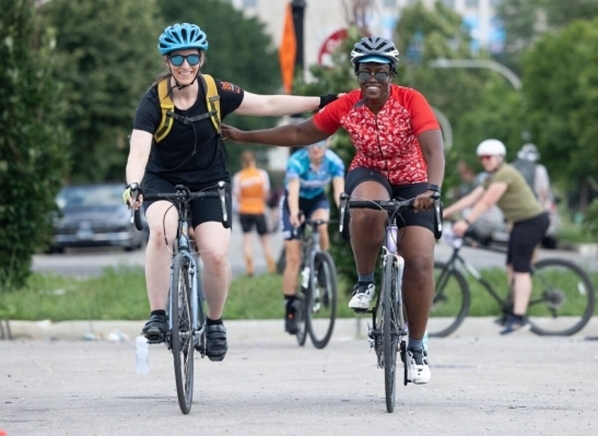 Two women on bikes reaching for each others backs in happy embrace.