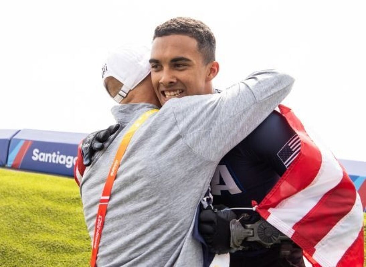 Man hugging cyclist who is wrapped in an American flag. USA Cycling is a non-profit organization accepting tax-deductible donations.