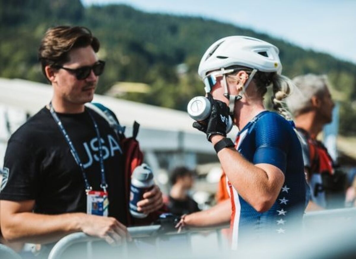 A USA cycling women athlete cooling her safe down with a bottle of water while chatting with a race official